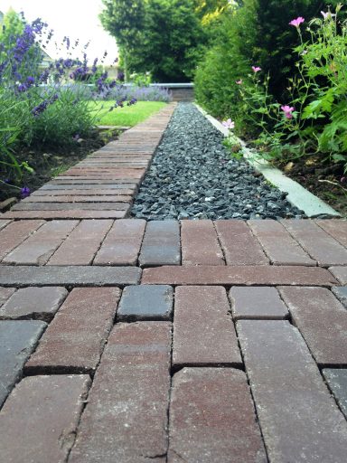 Een pad met stenen en grind, omringd door groene planten en bloemen.