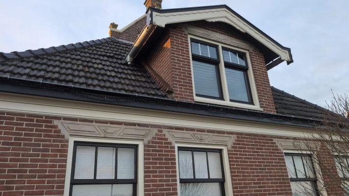Hoek van een traditioneel huis met een lichtgrijze bakstenen gevel en meerdere ramen.